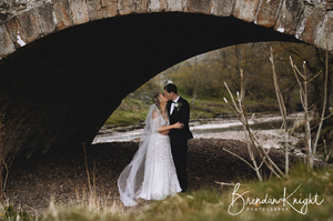 Bride and groom stood under an arched stone bridge