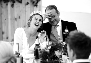 bride and groom laughing at farther of brides speech