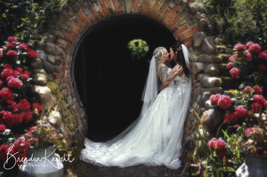 two brides in white dresses kissing in a round pick archway